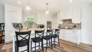 Una cocina moderna con armarios blancos, una isla central con taburetes y luminarias colgantes.