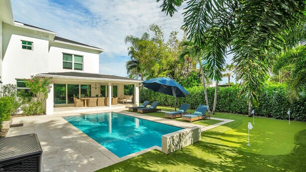 Una casa moderna con piscina, mobiliario de exterior y exuberante vegetación.
