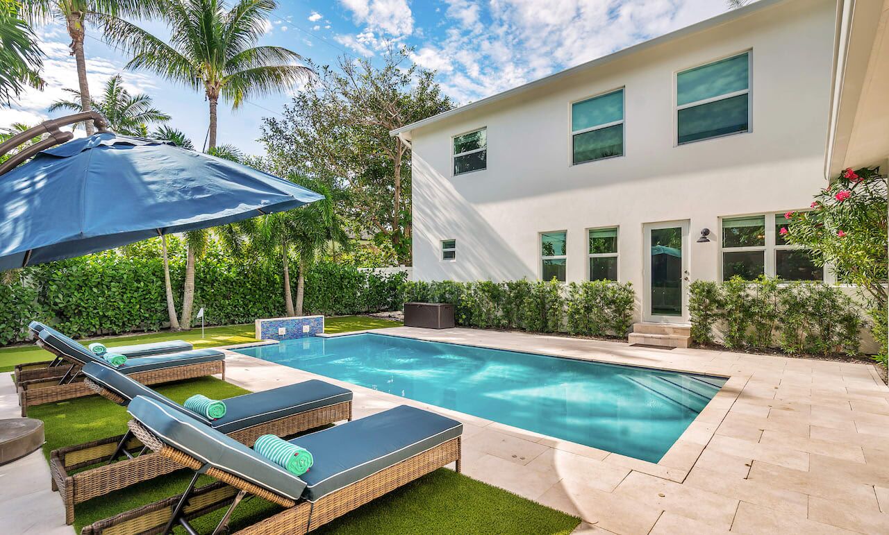 A modern house with a swimming pool, sun loungers, and a covered patio area.