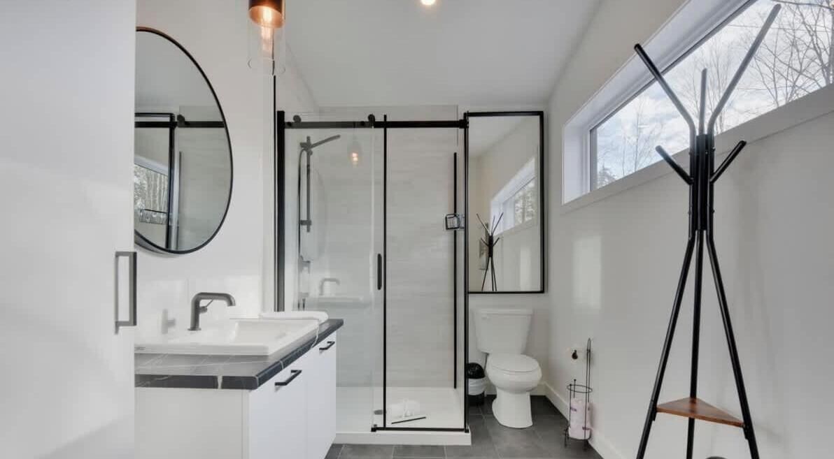 Un baño moderno con ducha envuelta en vidrio, inodoro y lavamanos con espejo.
