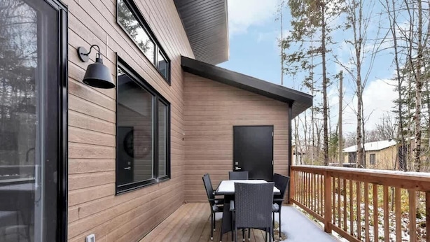 Un bâtiment moderne avec une façade en bois, une terrasse dotée de sièges extérieurs et une vue sur les arbres.
