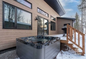 Una casa moderna con amplios ventanales, un jacuzzi y una terraza de madera.