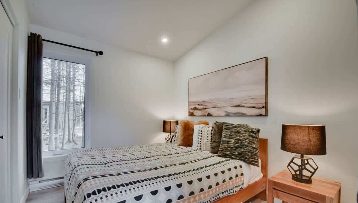 Een slaapkamer met een bed, een raam met gordijnen, een aan de muur hangend schilderij en een bedlampje.