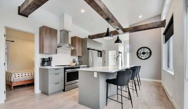 Una cocina moderna con una isla central, taburetes de bar y un reloj en la pared.