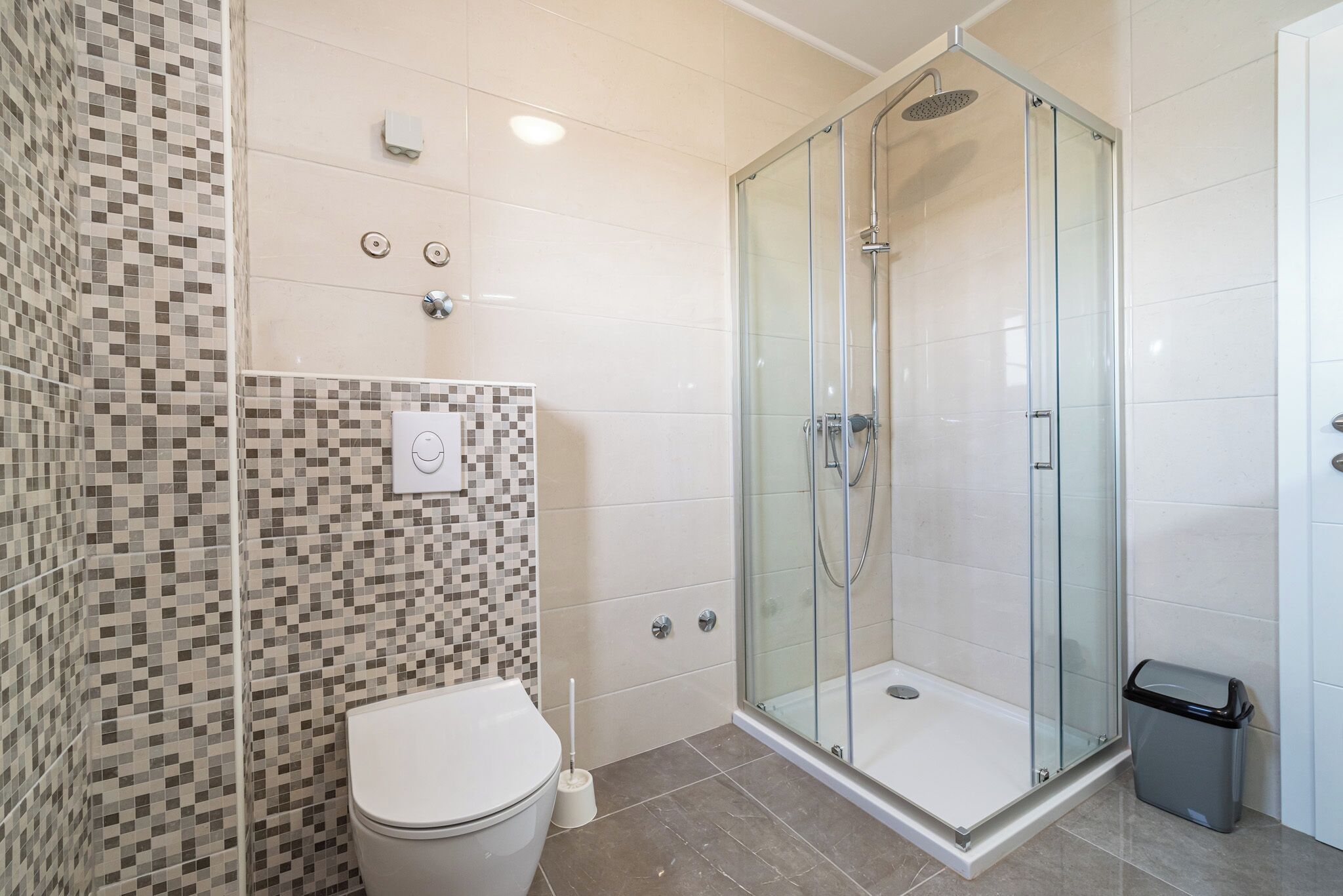 A modern bathroom with a glass-enclosed shower, a toilet, and a tiled wall.