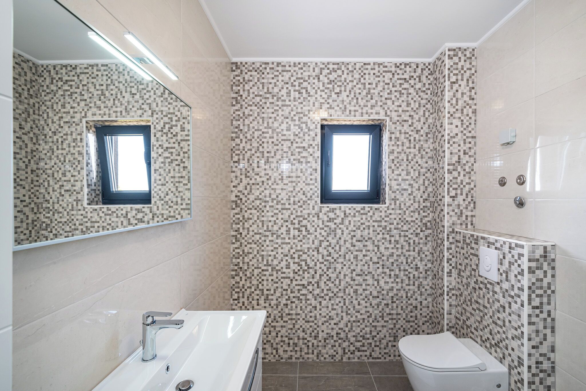 A bathroom with a tiled wall, a sink, a toilet, and a window.
