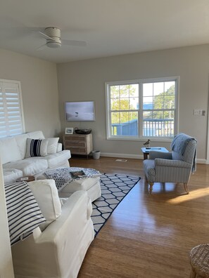 Una sala de estar con un sofá blanco, un sillón a rayas, un televisor y un ventanal con vistas al exterior.