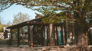 A rustic building with a glass enclosure, a stone wall, and a large tree in front. - Lost Ridge Inn & Brewery & Ranch (Sighnaghi)