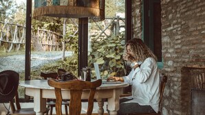 A person working on a laptop at a round wooden table with a rustic lamp overhead. - Lost Ridge Inn & Brewery & Ranch (Sighnaghi)