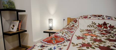 A neatly made bed with a floral-patterned bedspread, a bedside table with a lamp, and a bookshelf against the wall.