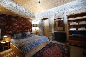 A bedroom with a bed, wooden headboard, patterned rugs, a wardrobe, and a stone wall. - Lost Ridge Inn & Brewery & Ranch (Sighnaghi)