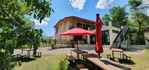 An outdoor seating area with tables and red umbrellas, a building with a staircase, and a clear sky. - Lost Ridge Inn & Brewery & Ranch (Sighnaghi)