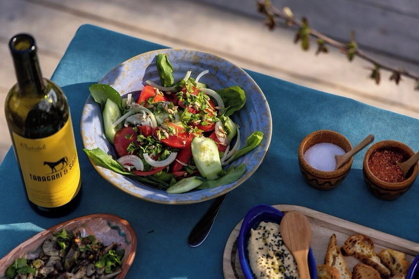 A table with a bowl of salad, a bottle of wine, and small bowls of condiments.