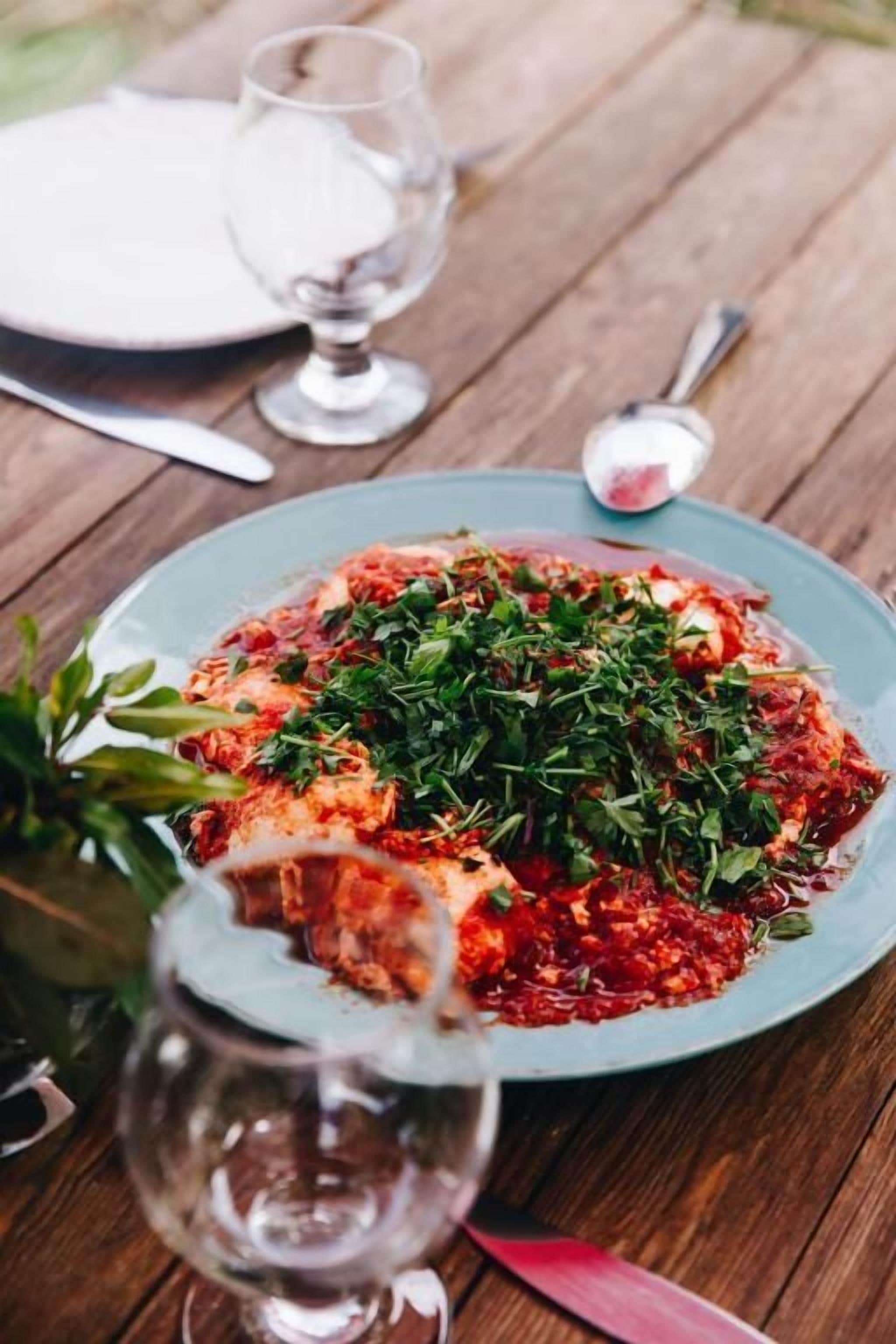 A plate of food on a wooden table with a glass of water and a spoon.