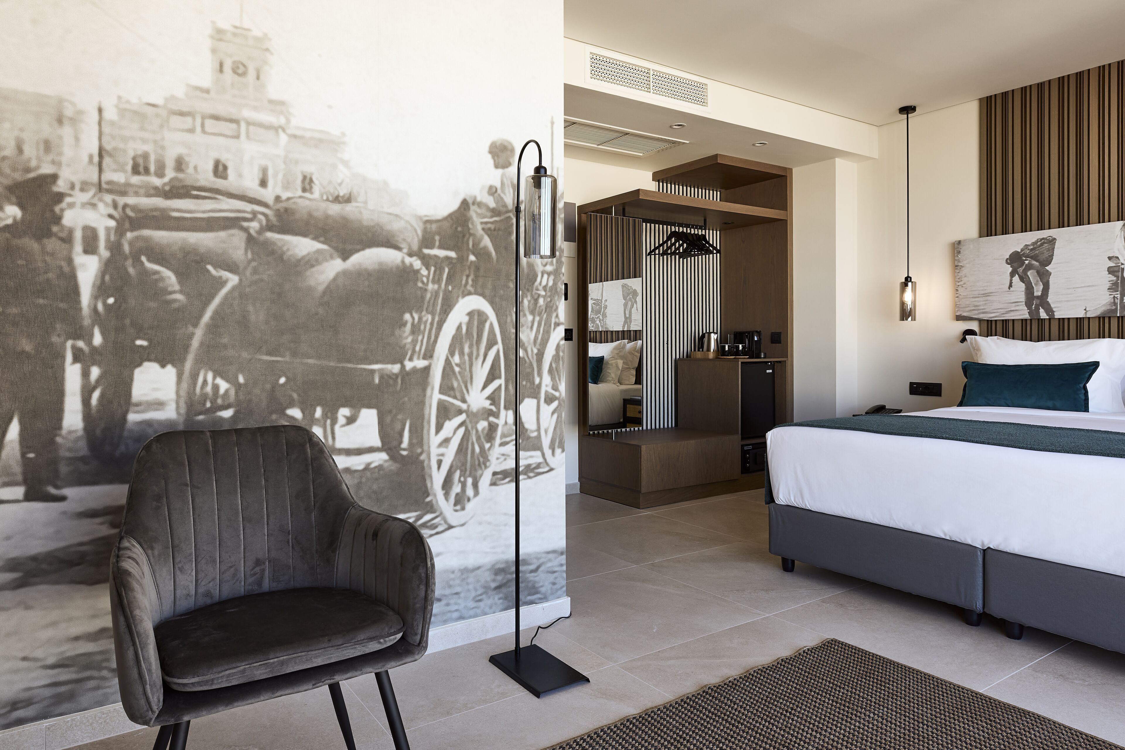 Une chambre d’hôtel moderne, dotée d’un grand lit, d’une chaise et d’une œuvre d’art fixée au mur, représentant une scène d’époque.