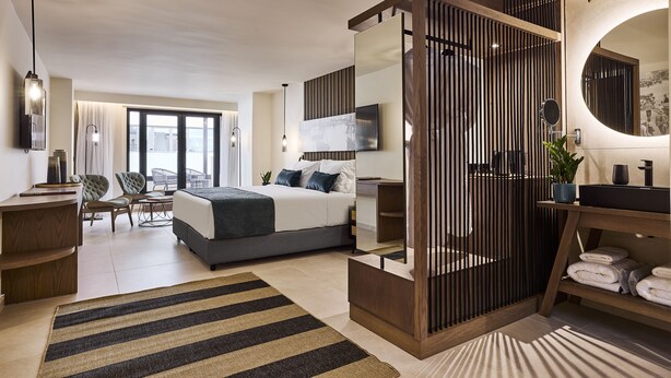 A modern hotel room with a large bed, a desk, a chair, a TV, and a bathroom with a mirror and sink. - Athenarum Portus Life & Style Hotel (Piraeus)