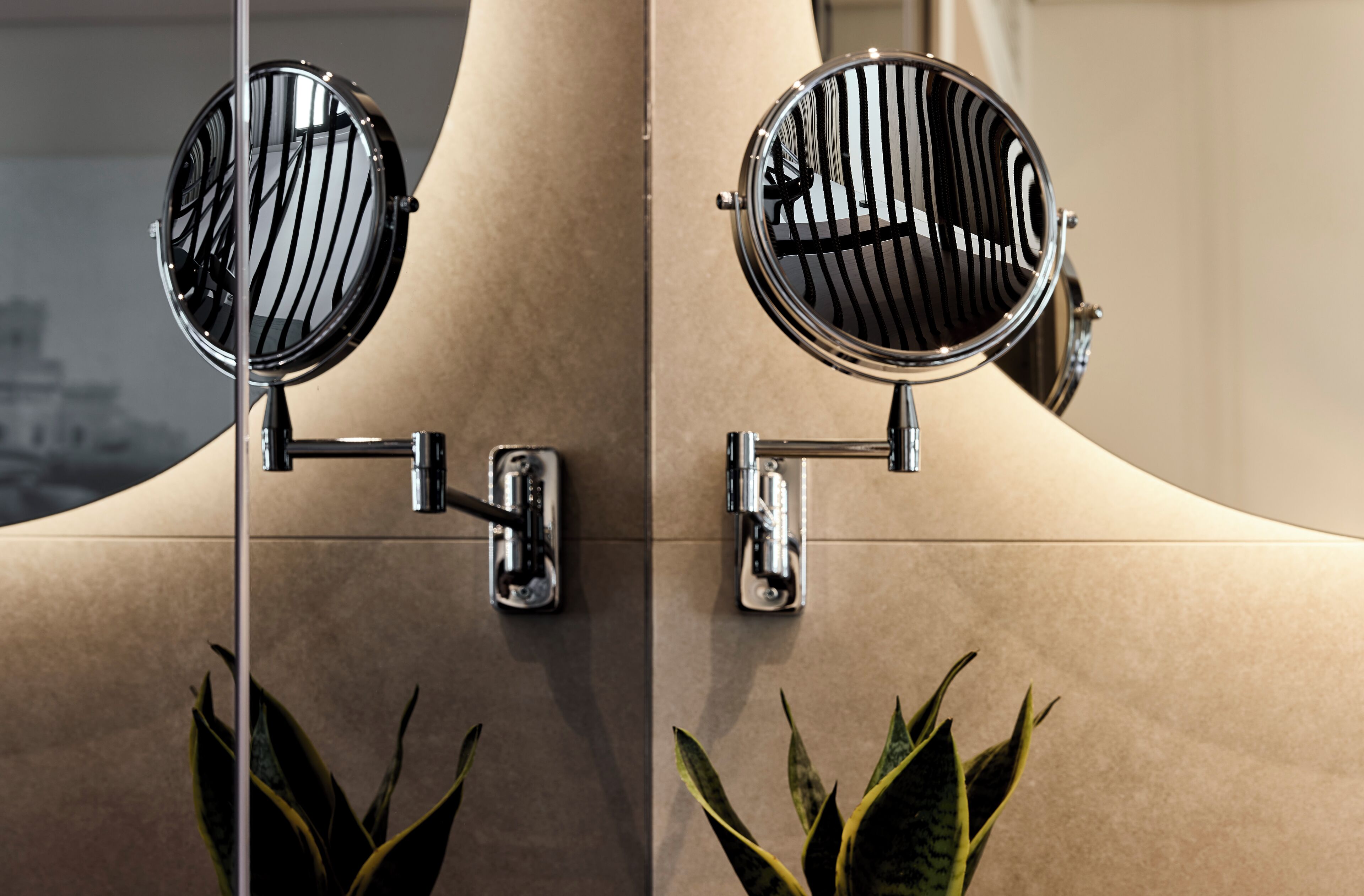 Un miroir mural avec un cadre chromé, fixé à un mur beige à l’aide d’une structure de support verticale.