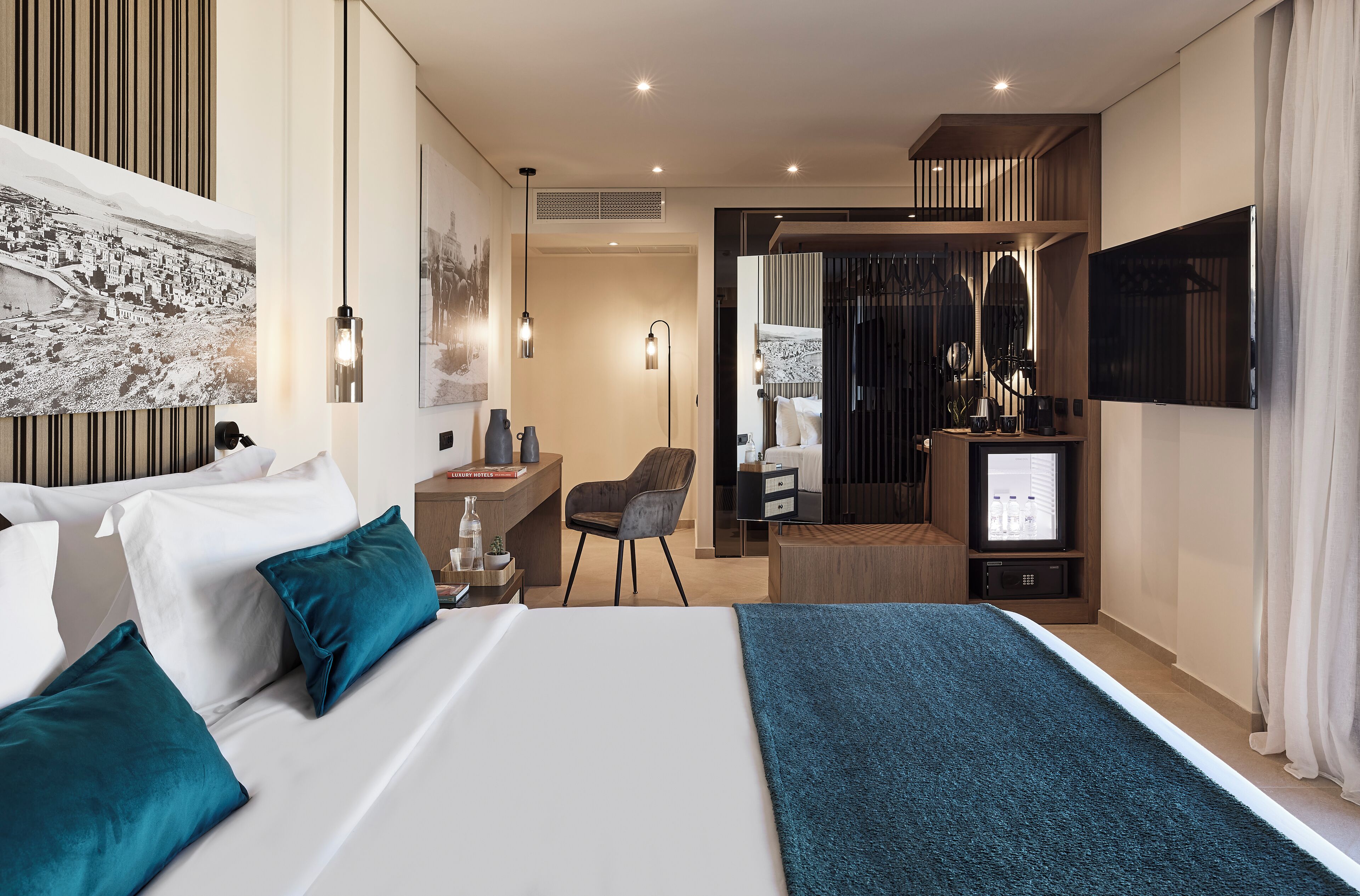 A modern hotel room with a large bed, a desk, a chair, a TV, and artwork on the walls.