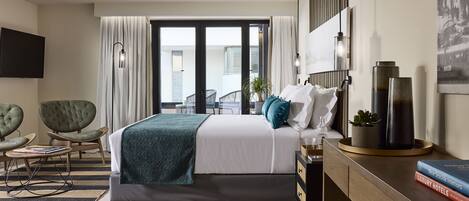 A modern hotel room with a large bed, a desk, a chair, and a view of the city through the window.