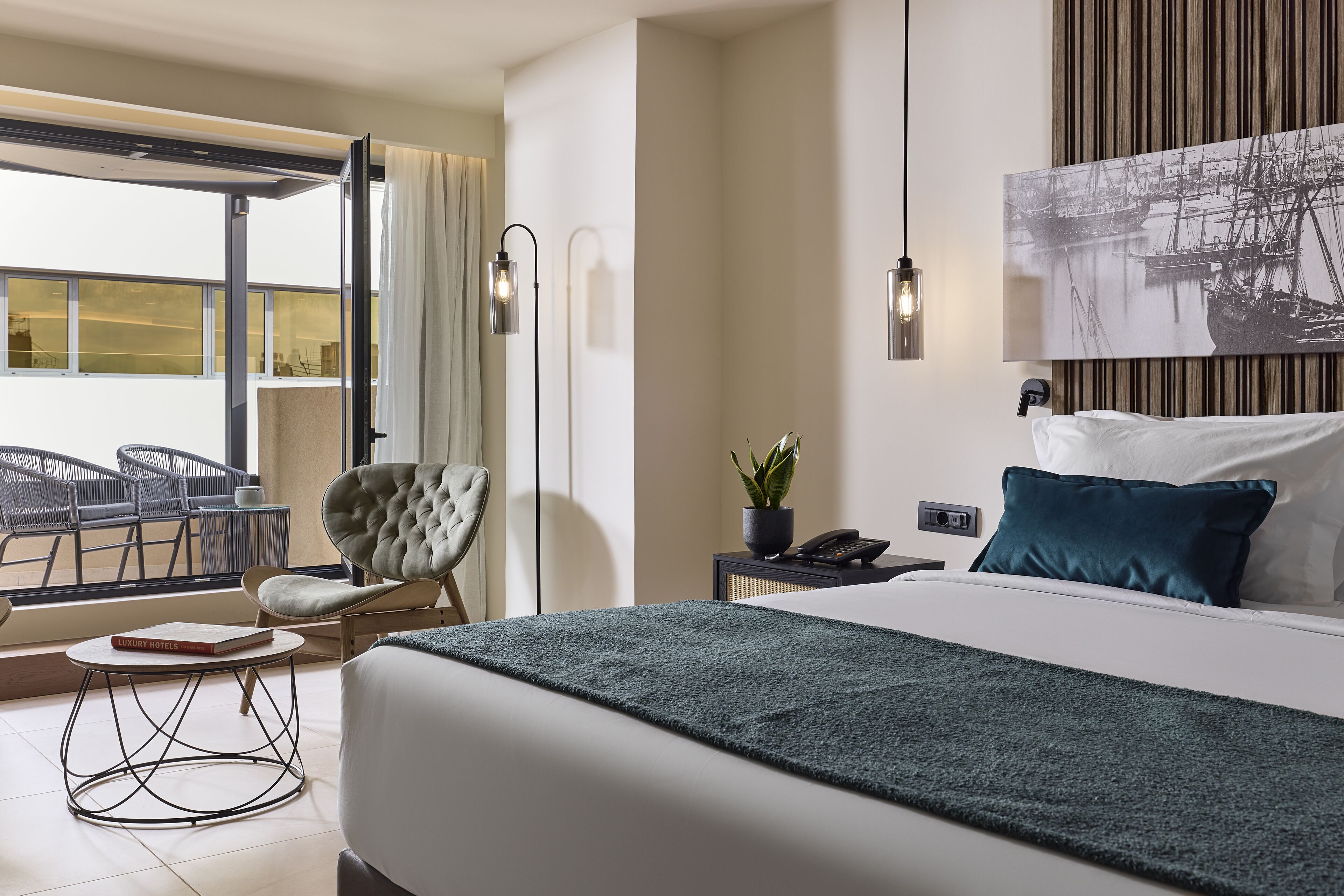 Habitación de hotel con cama, una silla, una mesa, una planta y vistas al exterior.
