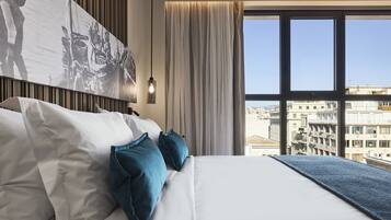 Quarto de hotel com uma cama grande, vista de edifícios pela janela e uma obra de arte na parede.
