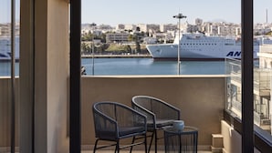 A balcony with two wicker chairs and a small table, overlooking a marina with a large ship. - Athenarum Portus Life & Style Hotel (Piraeus)
