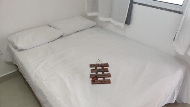 A neatly made bed with white linens and a wooden sign on the bed. - Pousada Sonho Meu Itaunas (Conceicao da Barra)