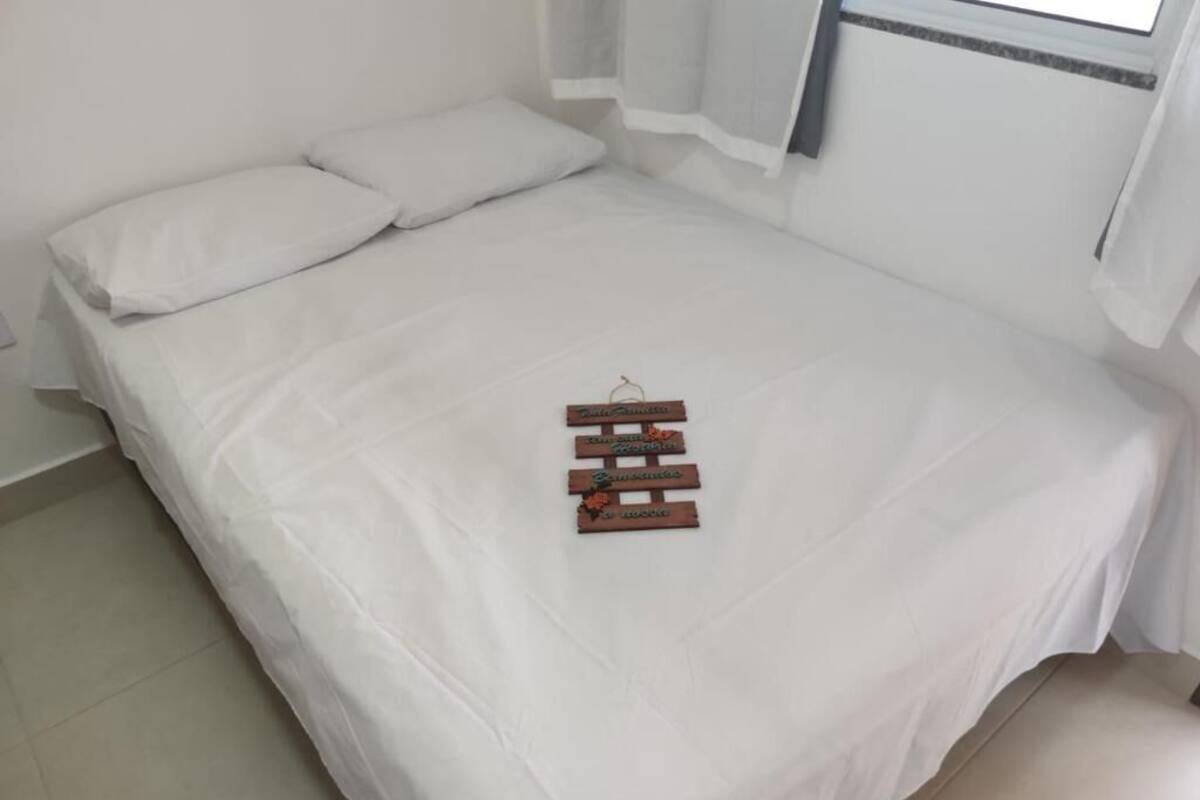 Ein ordentlich bezogenes Bett mit weißen Leinen und einem Holzschild darauf.