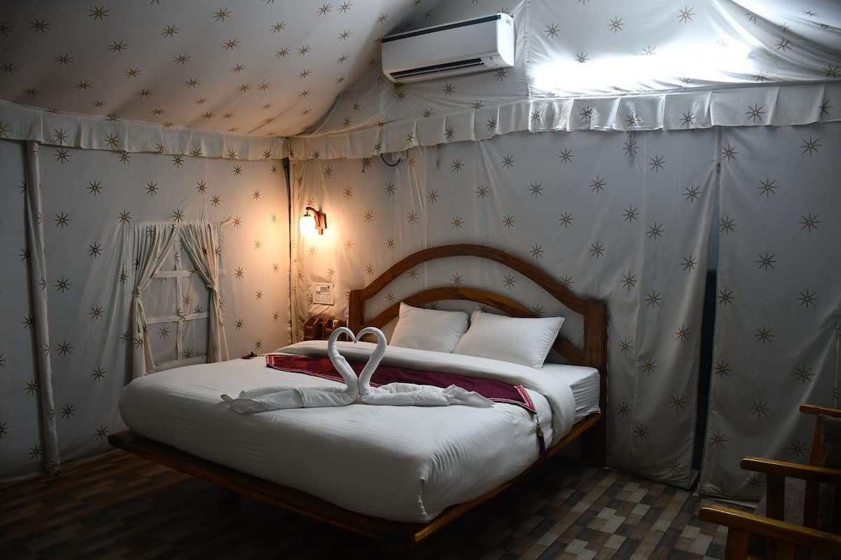 Un dormitorio con cama, cabecera de madera, aire acondicionado de pared y cortina estampada.