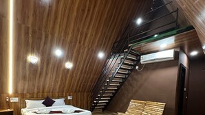 Una habitación con techo inclinado, piso de madera, una cama con ropa de cama blanca, un banco de madera y una escalera.