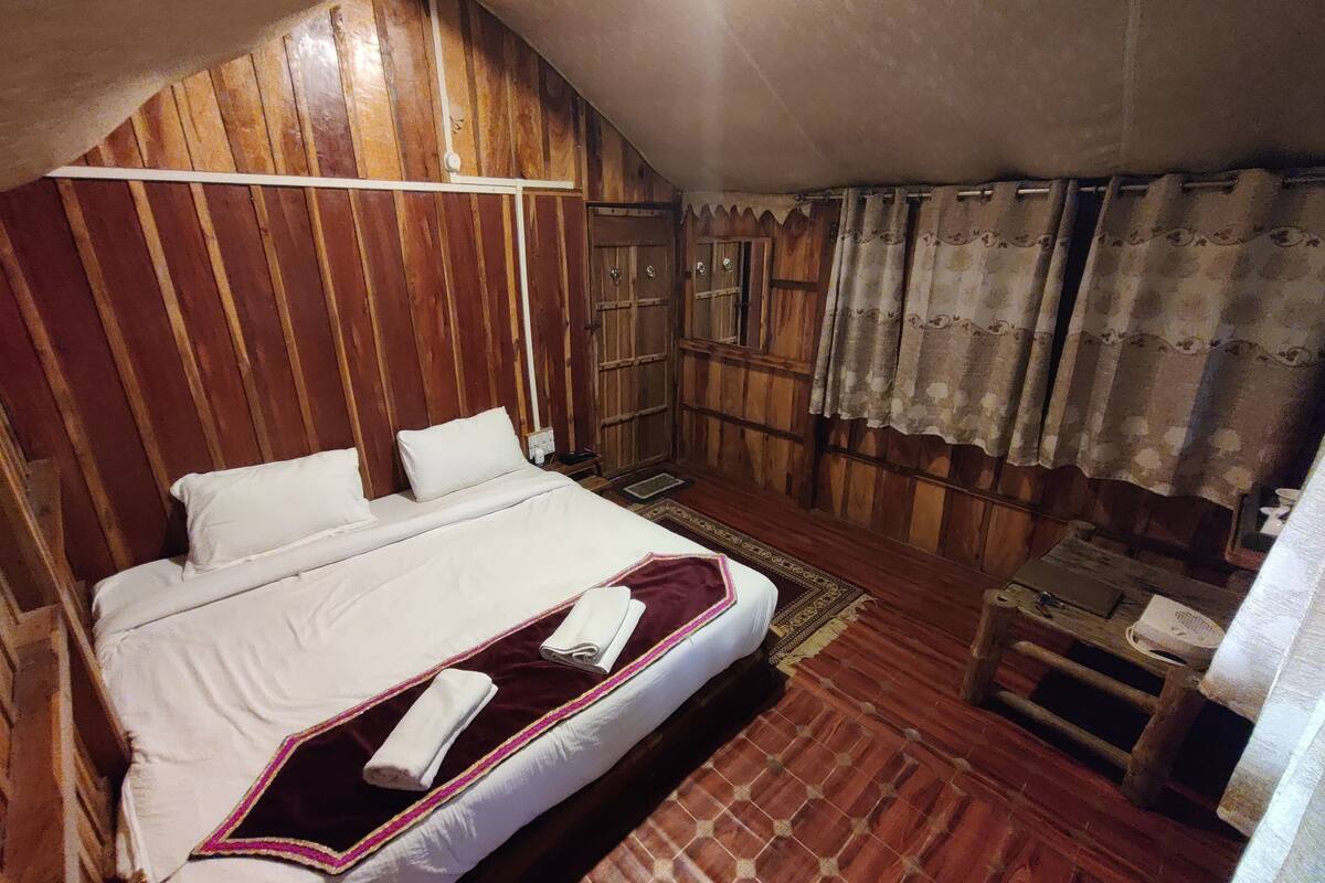 Un dormitorio con techo inclinado de madera, una cama con ropa blanca, una manta roja y blanca, y piso de madera.