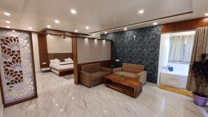 Una habitación de hotel moderna con una cama grande, un sofá, una mesa de centro y un baño visible a través de una ventana.