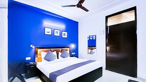 A modern bedroom with a large bed, a ceiling fan, and a door with a dark frame. - Roomshala 141 Agniv Residency (New Delhi)