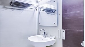A bathroom with a pedestal sink, a mirror, and a towel rack. - Roomshala 141 Agniv Residency (New Delhi)