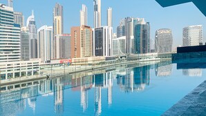 Le profil d’une ville se reflète dans une étendue d’eau calme, avec en arrière-plan des immeubles modernes de grande hauteur.