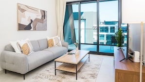 Un salon moderne avec un canapé gris, une table basse en bois et une grande fenêtre donnant sur des immeubles.