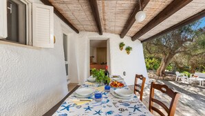 An outdoor dining area with a table set for two, surrounded by wooden chairs, under a wooden beam roof. - 3677 Trullo Foresta Forte by Barbarhouse (Castrignano del Capo)