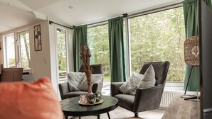 Un salon moderne avec deux fauteuils gris, une table basse ronde et une grande fenêtre ornée de rideaux verts.