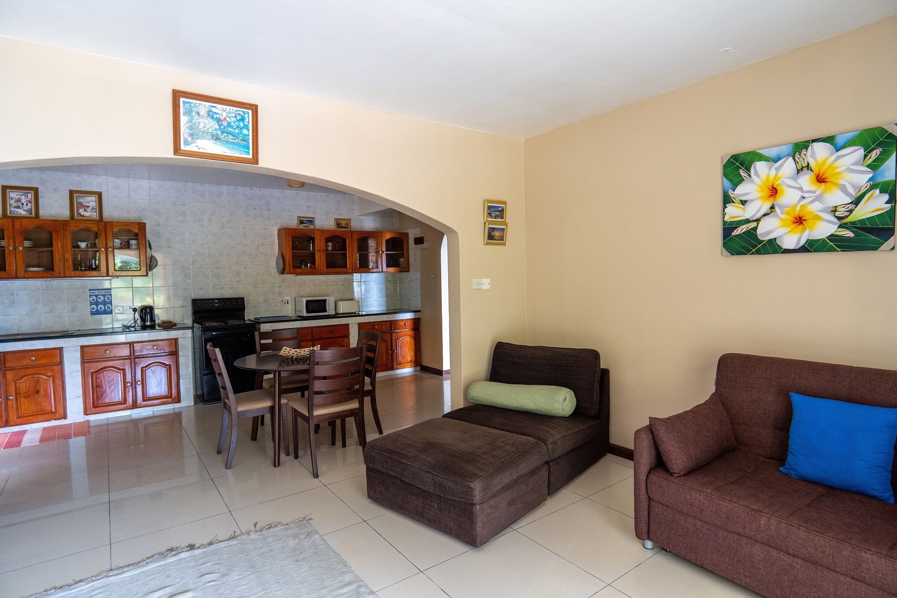 A living room with a sofa, a dining area with chairs, a kitchen with cabinets and appliances, and a painting on the wall.