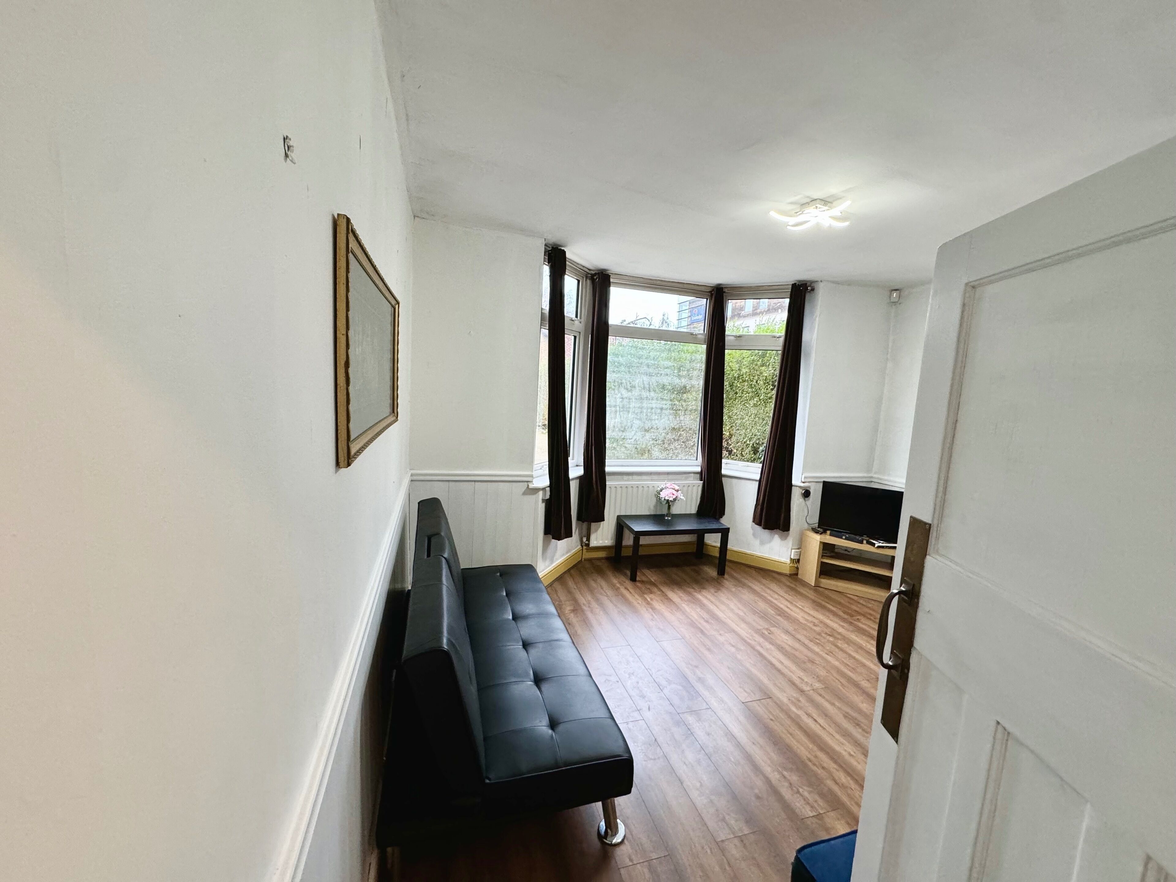 A room with a black sofa, a small table, a TV, and a window with curtains.