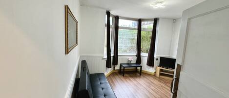 A room with a black sofa, a small table, a TV, and a window with curtains.