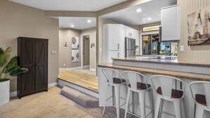 Une cuisine moderne avec des meubles blancs, un réfrigérateur en acier inoxydable et un coin bar doté de tabourets de bar blancs.