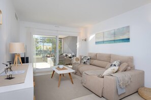 A modern living room with a sofa, a coffee table, and a lamp. There is a painting on the wall and a view of the outdoors through a glass door. - Fidalsa Utopia junto al mar (Punta Prima)