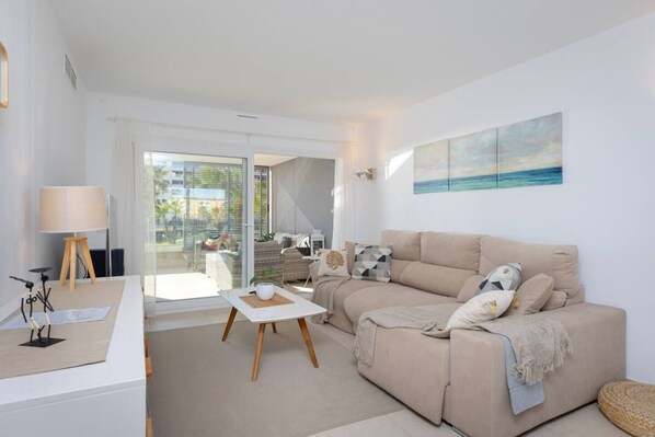 A modern living room with a sofa, a coffee table, and a lamp. There is a painting on the wall and a view of the outdoors through a glass door. - Fidalsa Utopia junto al mar (Punta Prima)