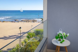 Ein Balkon mit Blick auf einen Strand und das Meer, ein kleiner Tisch mit einer Pflanze und ein weißer Laternen.