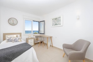 Ein Schlafzimmer mit einem Bett, einem Schreibtisch, einem Stuhl und Blick aufs Meer.