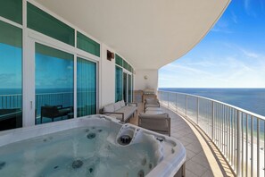 A balcony with a hot tub, outdoor seating, and a view of the ocean.