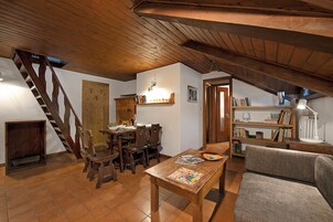 Acogedor cuarto ático con una escalera de madera, una mesa de comedor con sillas, un sofá y una estantería.