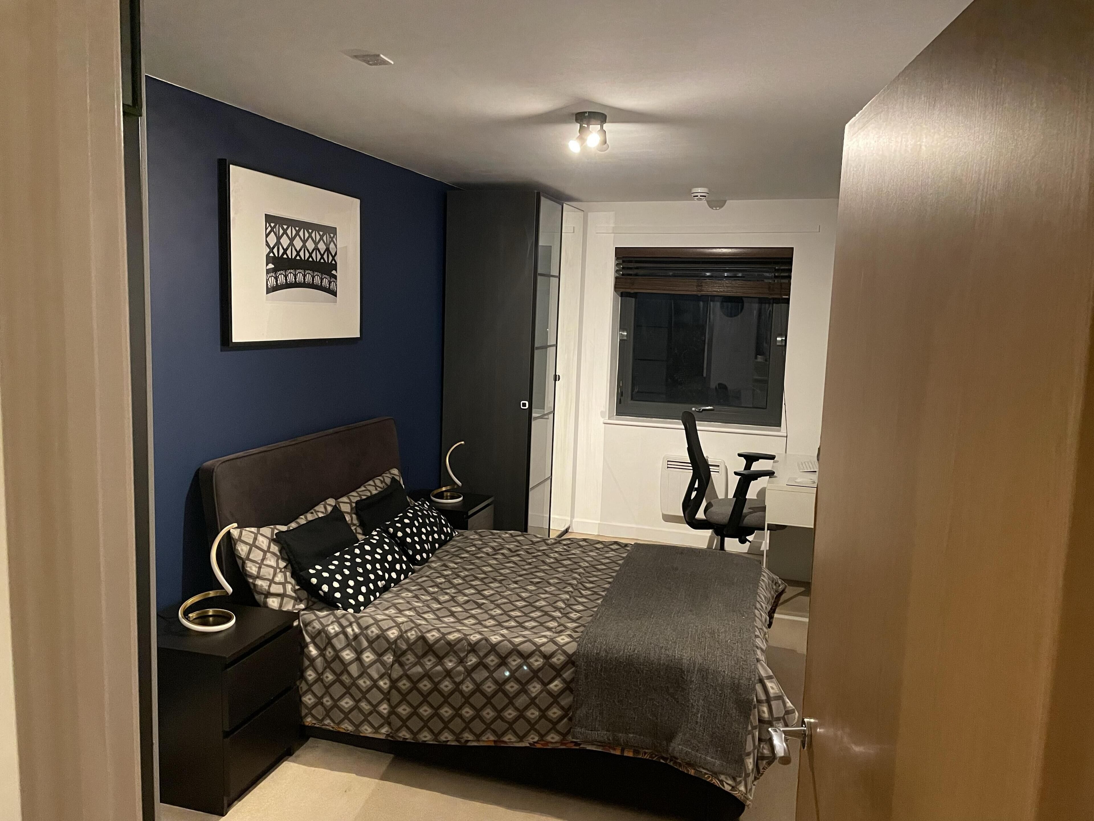 A bedroom with a bed, a desk, a chair, a window, and a door.