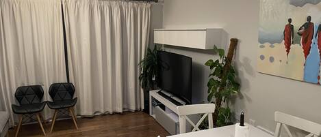 A living room with a TV, two black chairs, a white table, and a painting on the wall.